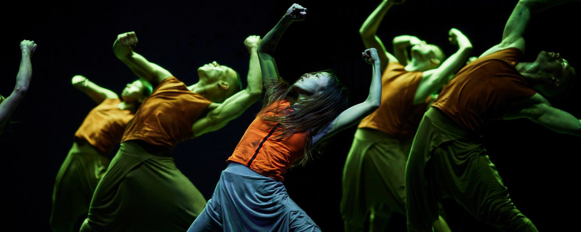group of dancers on stage leaning back with arms in the air with green lighting
