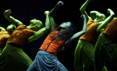 group of dancers on stage leaning back with arms in the air with green lighting