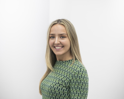 Headshot of Amelia Bickley. White blonde female smiling at the camera wearing green patterned top 