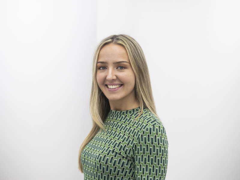 Headshot of Amelia Bickley. White blonde female smiling at the camera wearing green patterned top 