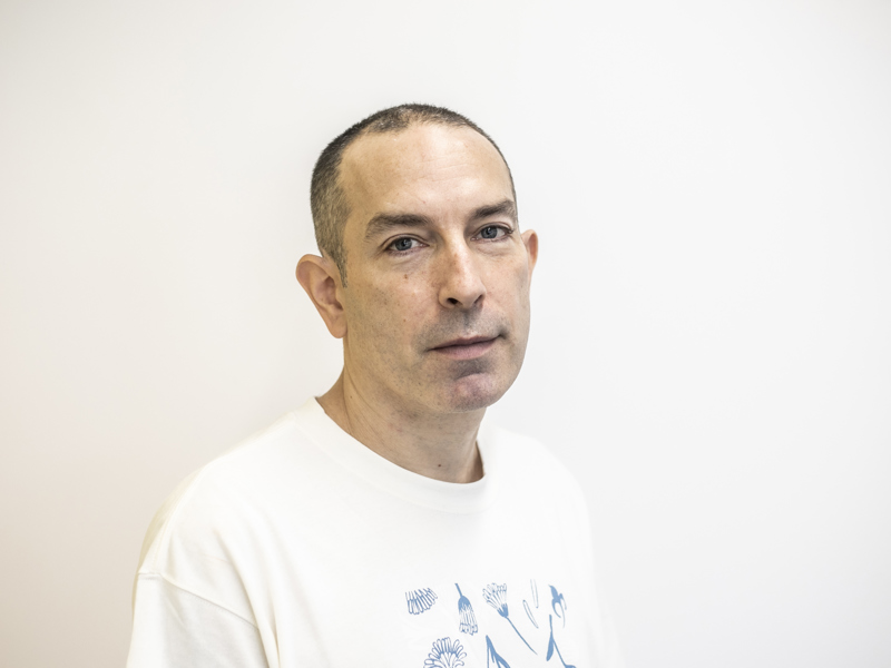 Headshot of Barny Darnell. White male with shaved head and white t-shirt with white background