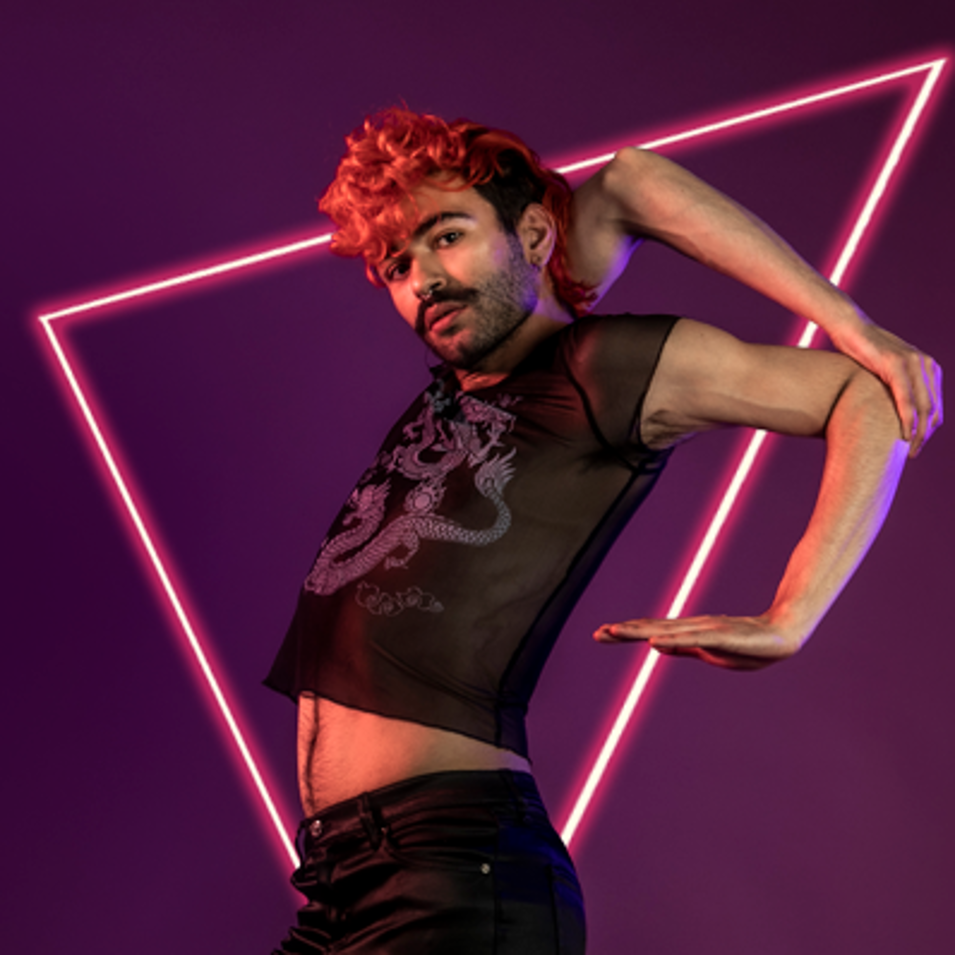 LGBTQ+ voguing dancer with curly red mohawk and black beard, holding onto his elbow. Wearing see-through black top on purple photo backdrop.