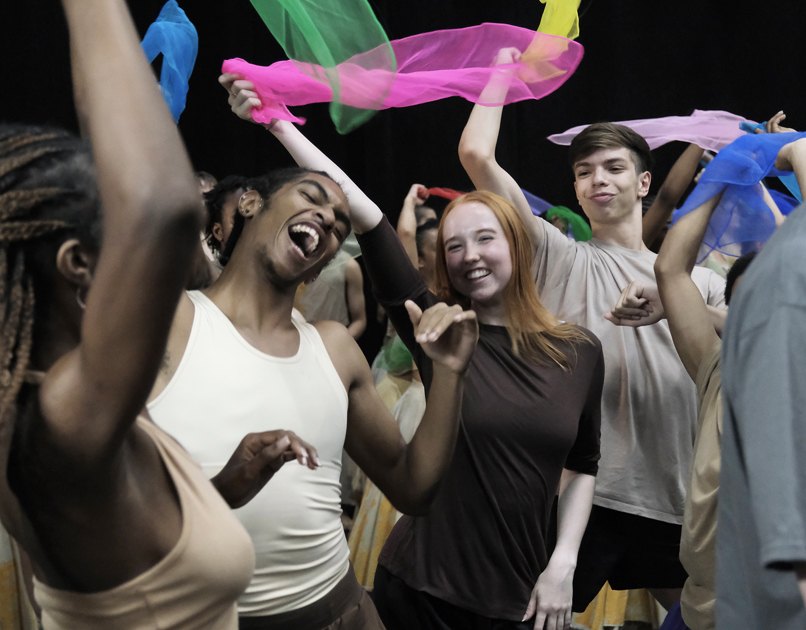 young people mixed genders and races dancing together with big smiling faced waving brightly colour scarfs. 