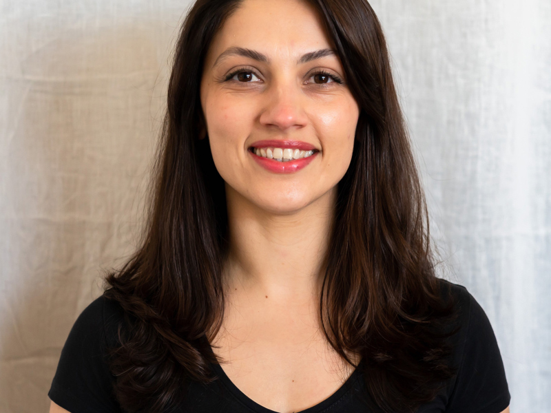 Headshot of Markella Kefallonitou. White female with long black hair smiling at the camera, wearing black t-shirt