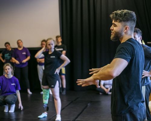 white male dancer guestering to dance students in a blacked out dance studio