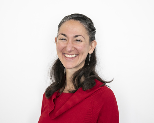 Headshot of Erin Sanchez. female with short brown smiling at the camera wearing red jumper with white background