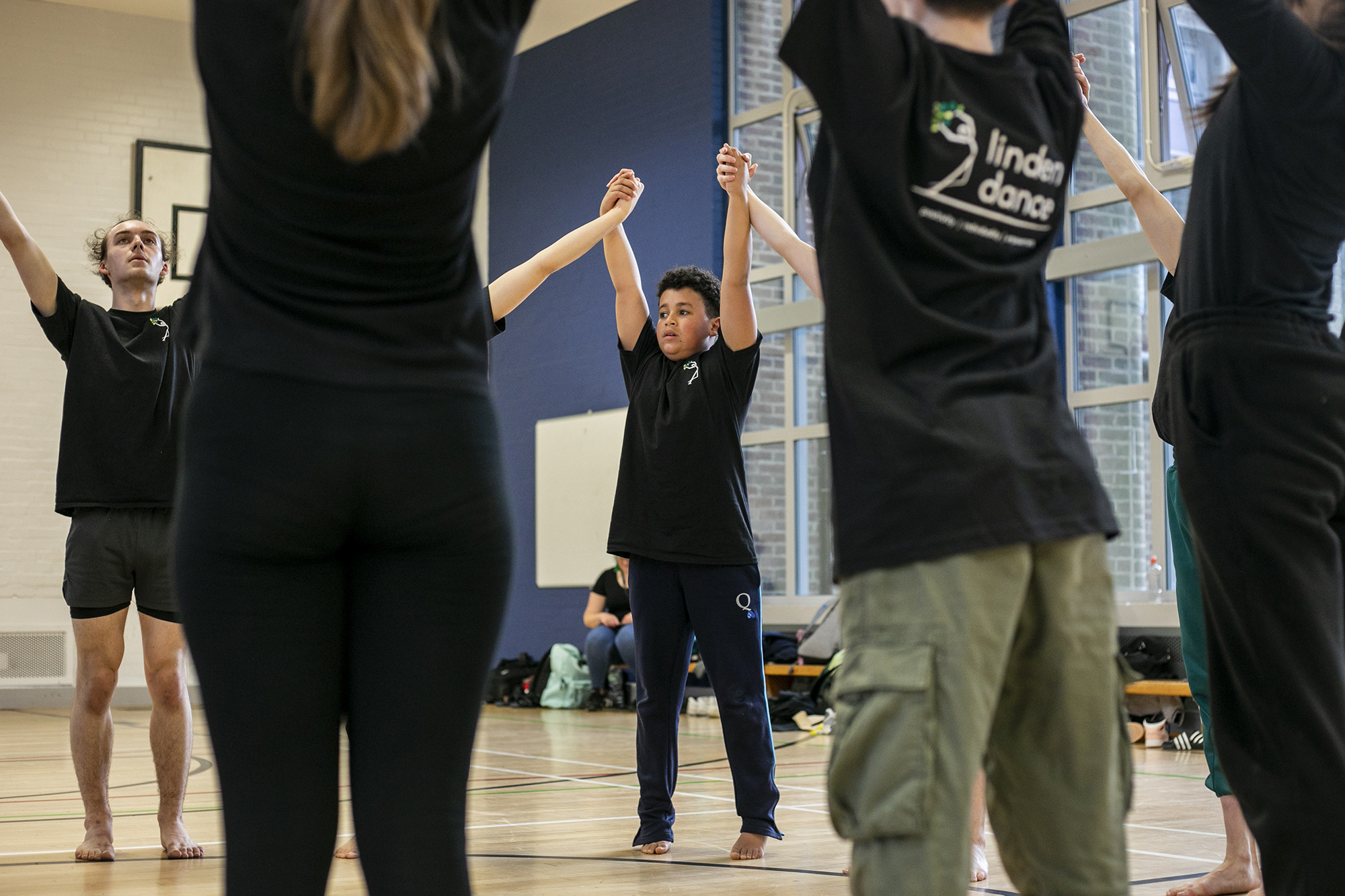 Dance circle with young people holding hands with the joint hands in the air. All wearing black PE kit in a sports hall. Dance circle with young people holding hands with the joint hands in the air. All wearing black PE kit in a sports hall.