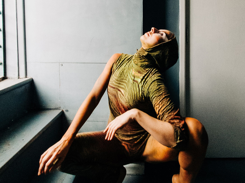 Image of Helen Calcutt. White female squatted down looking to the top left wearing green one sleeved leotard with a hood. 